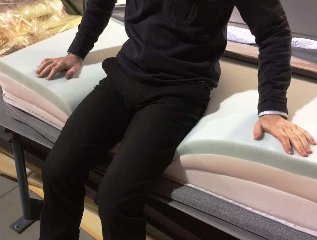 A man sitting on a side of a mattress without firm edges